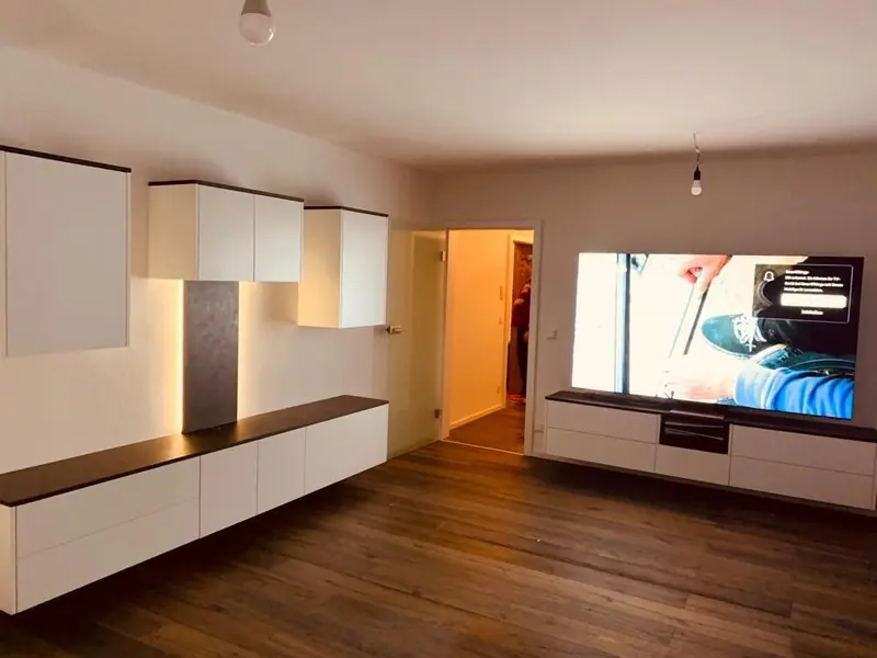 Weiße Hängeschränke mit Beleuchtung und ein Sideboard mit dunkler Platte im Wohnraum