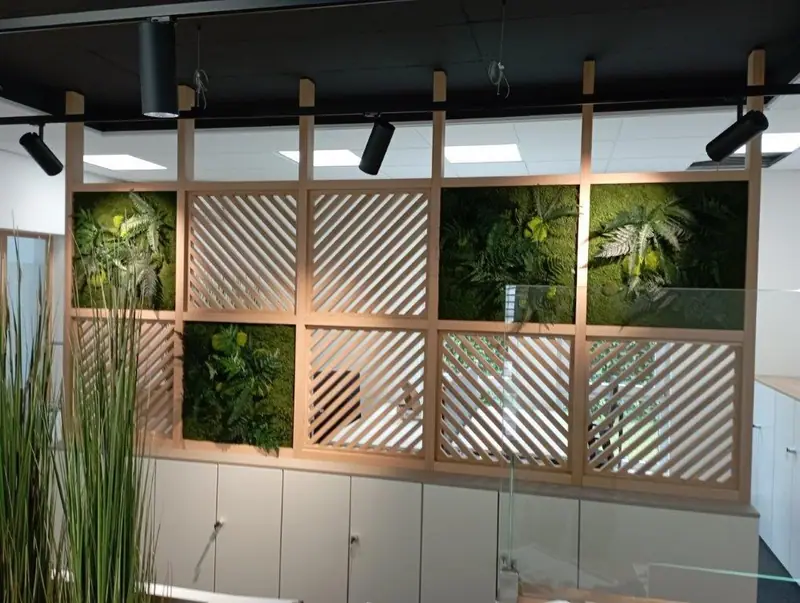 Raumteiler mit Holzlamellen vor einer Pflanzenwand in einem hellen Büro